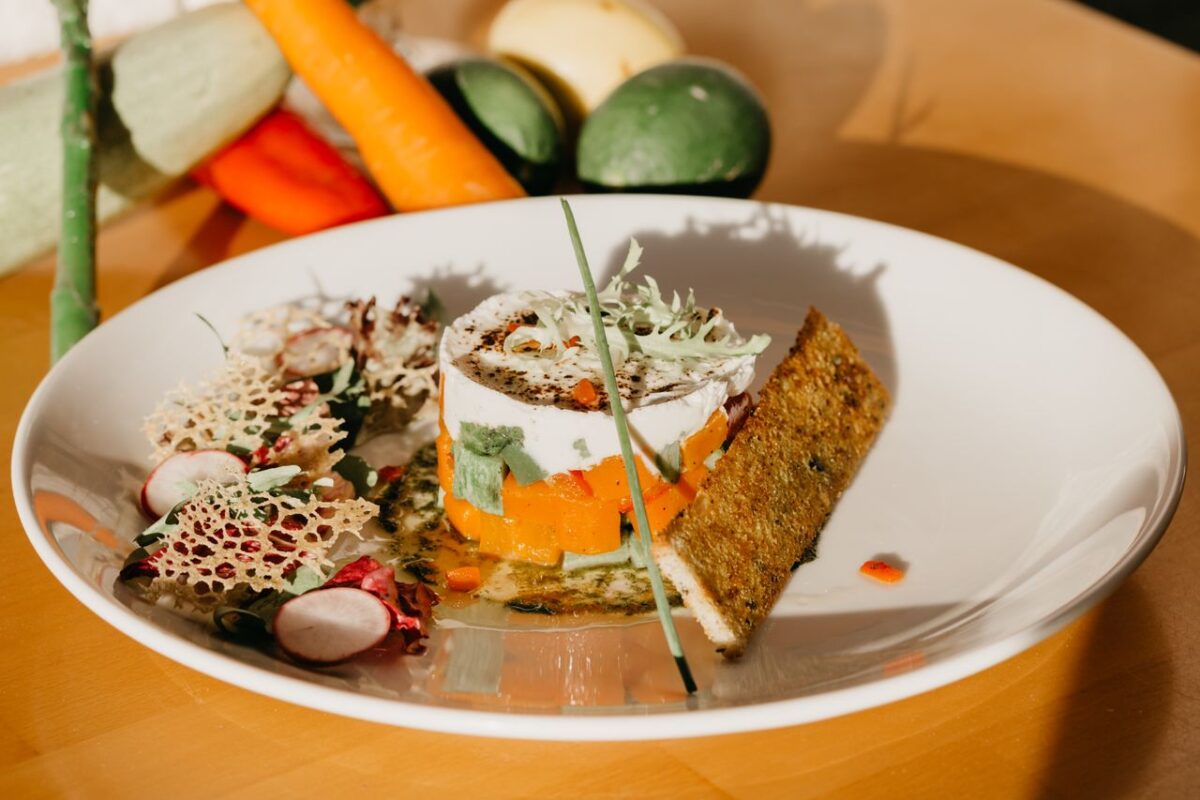 High angle of healthy vegetable tartar served on white ceramic plate with salad and crispy bread near scattered fresh ingredients in kitchen in sunlight